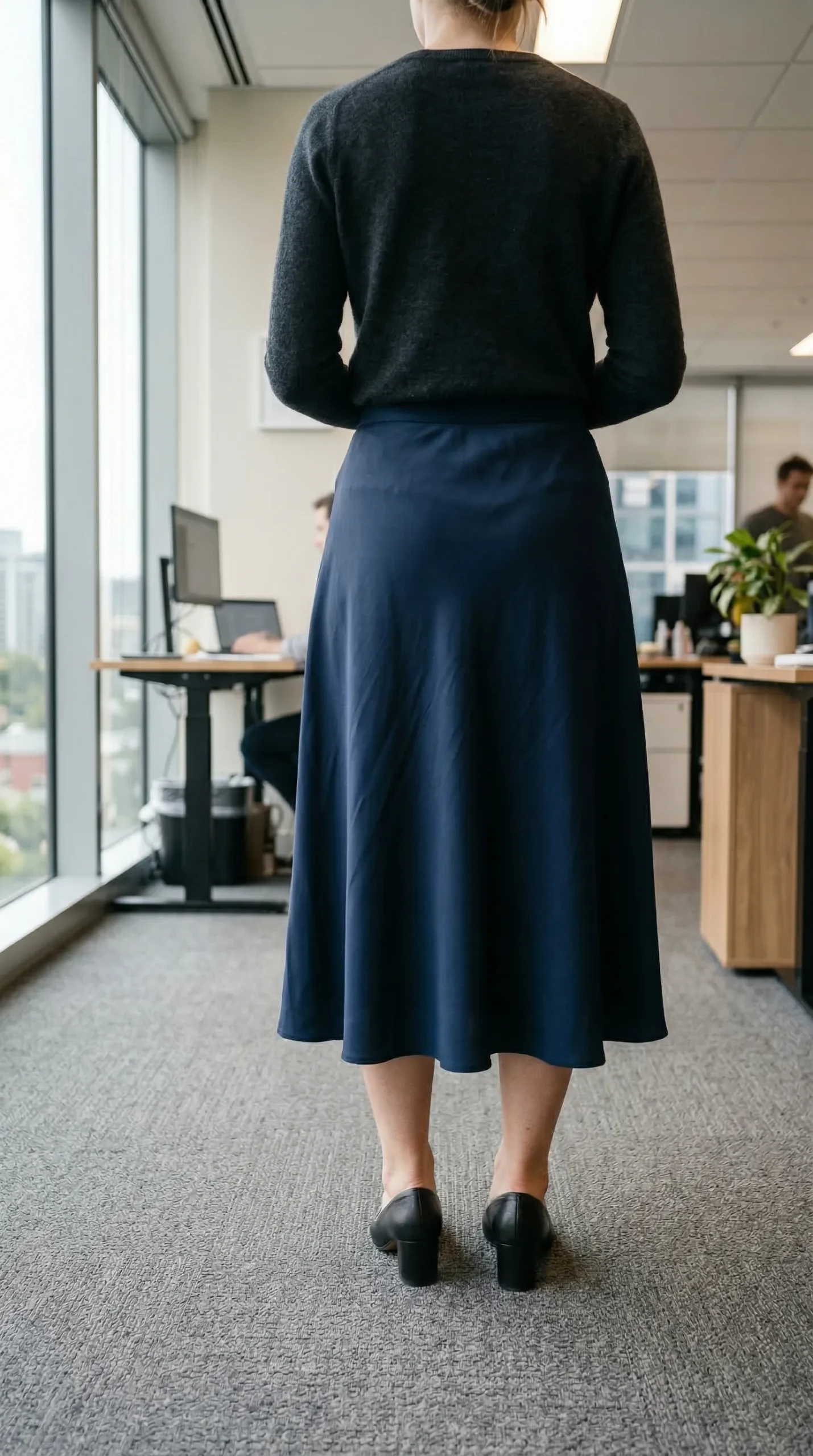 Woman from behind wearing a navy midi skirt that lands below the calf fullness — the universally leg-lengthening hem point