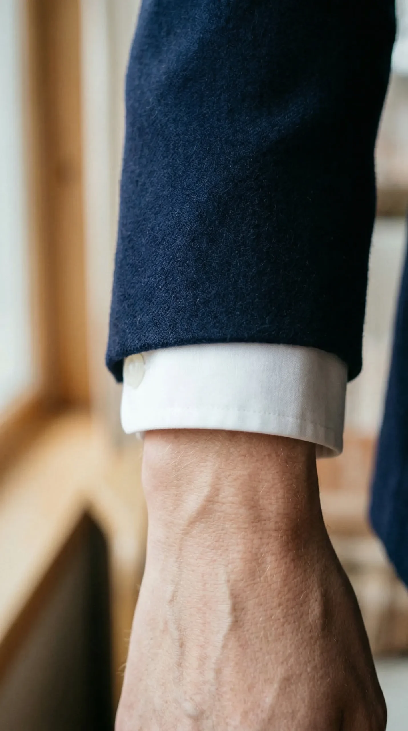 Close-up of wrist showing navy blazer sleeve ending at wrist bone with 1.5cm of white shirt cuff visible