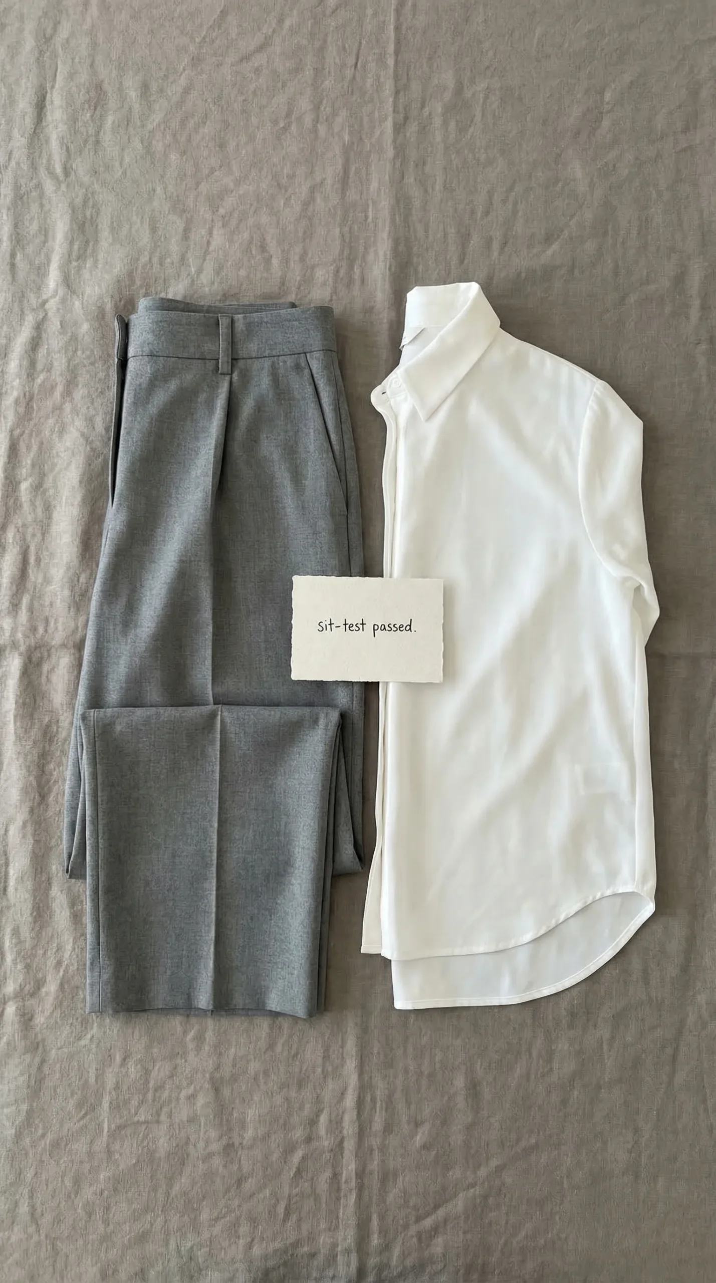 Flat lay of two anchor pieces — mid-grey wide-leg tailored trousers and a crisp white longer-back-hem blouse
