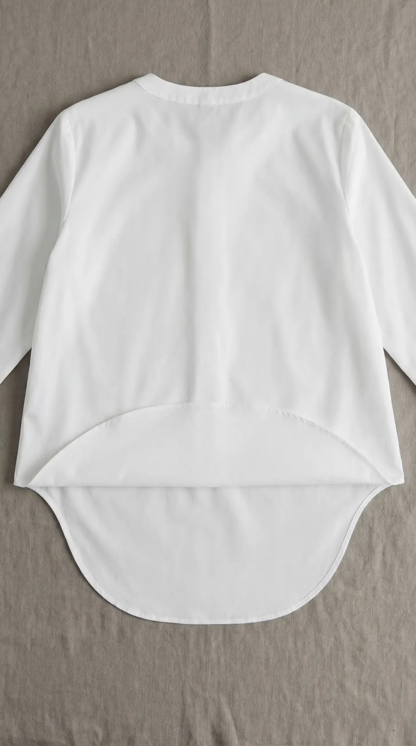 White blouse laid flat from behind showing the visibly longer curved back hem — the seated fabric reserve
