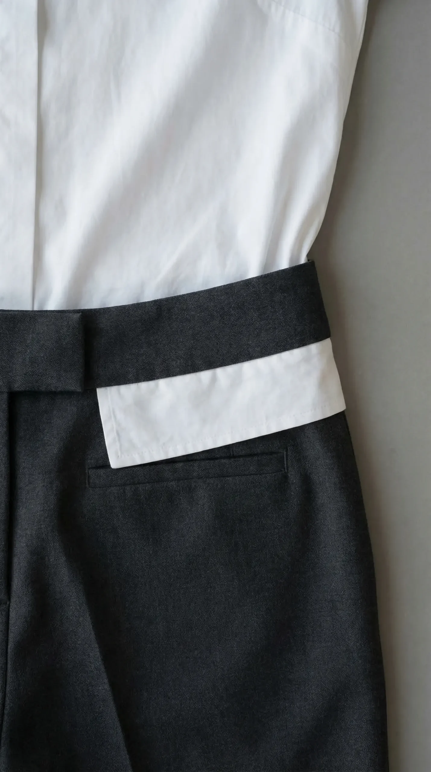 Close-up of white blouse tucked into dark grey trousers showing the 7cm fabric reserve below the waistband